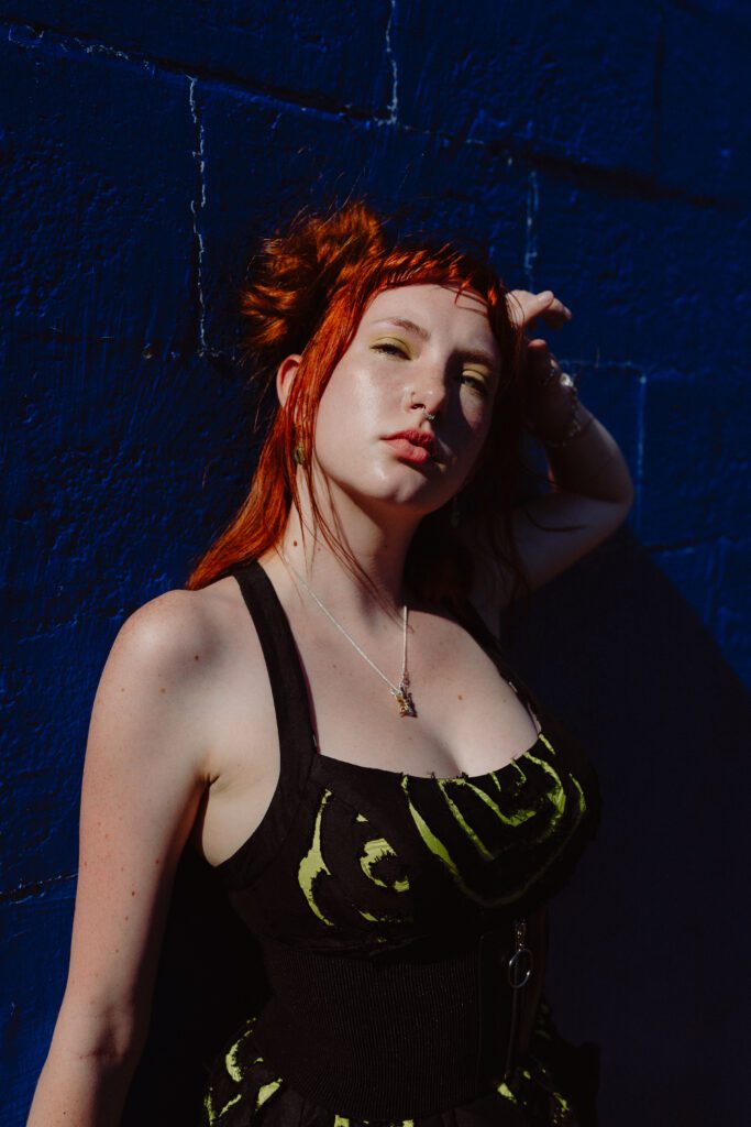 Woman posing in shadowy light against a dark blue wall, creating a moody editorial portrait with strong summer sun in Portland.