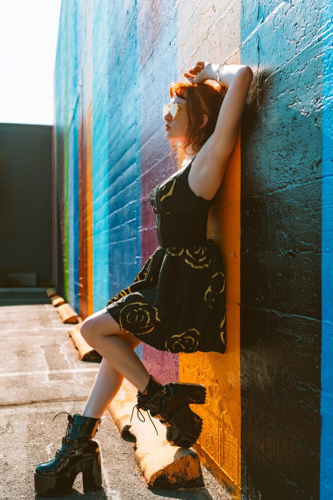 Client leaning back against a multicolor mural wall in heels and patterned dress, showcasing creative movement and playful styling in a vibrant Outdoor Adventure shoot in Portland, Oregon