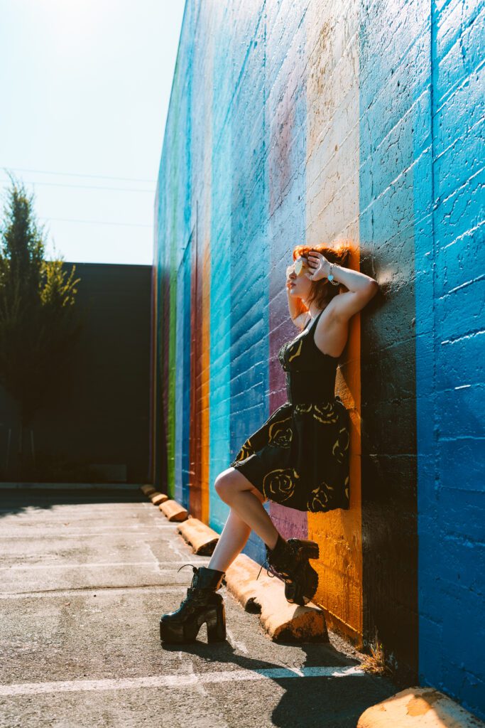 Woman leaning against a bold blue wall with rainbow tones and dramatic sunlight in a creative brand photography session on Portland’s Eastside.