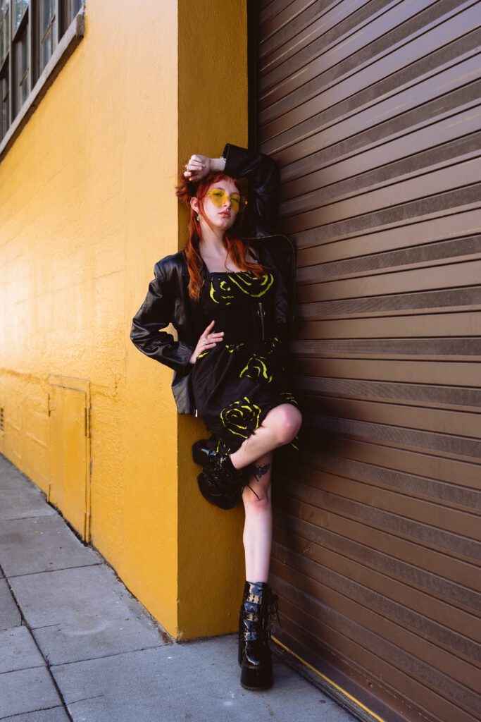 Woman leaning against a corrugated brown and yellow wall in boots and jacket during a bold editorial-style shoot in Eastside Portland photography session