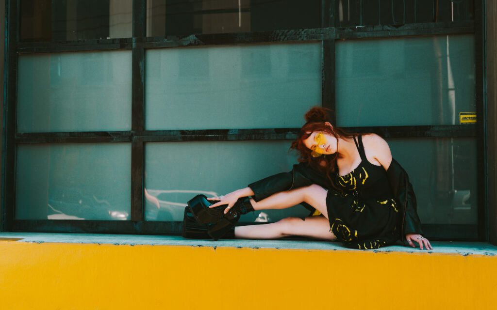 Creative branding photo of a woman reaching across a yellow ledge in front of a modern building facade during a styled Portland photo session.