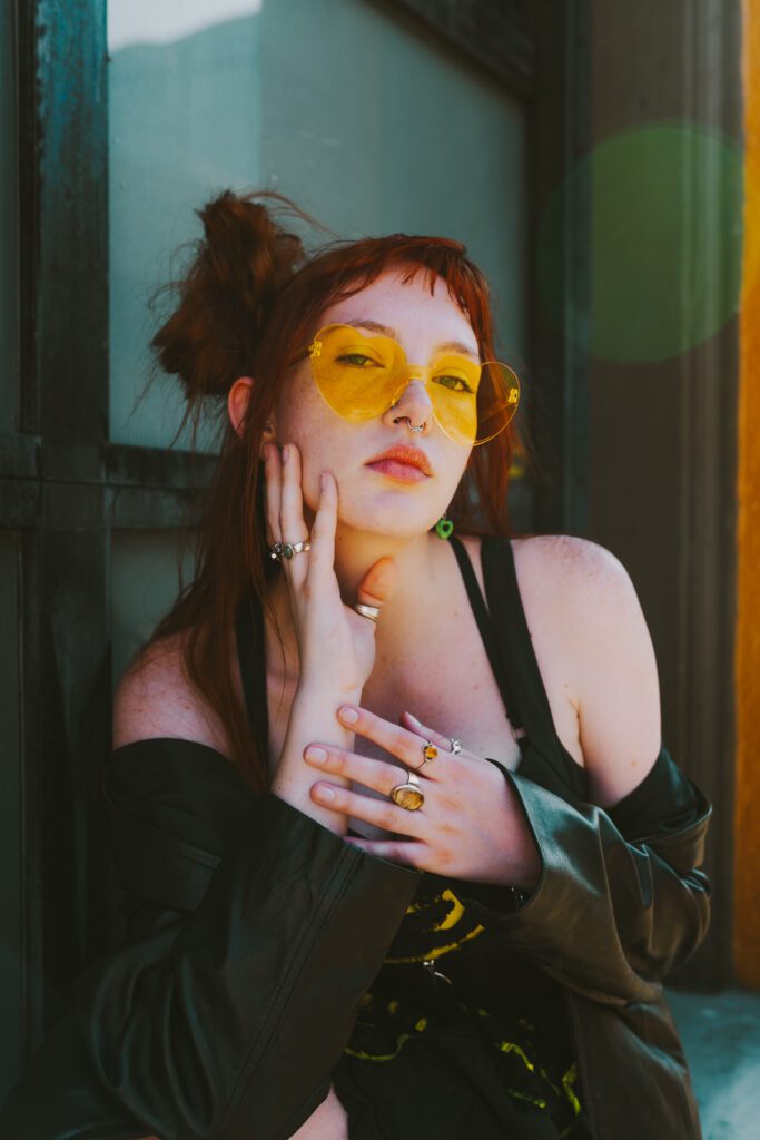 Close-up of a woman wearing yellow-tinted sunglasses, framed in soft directional light during a vibrant editorial shoot in Portland.