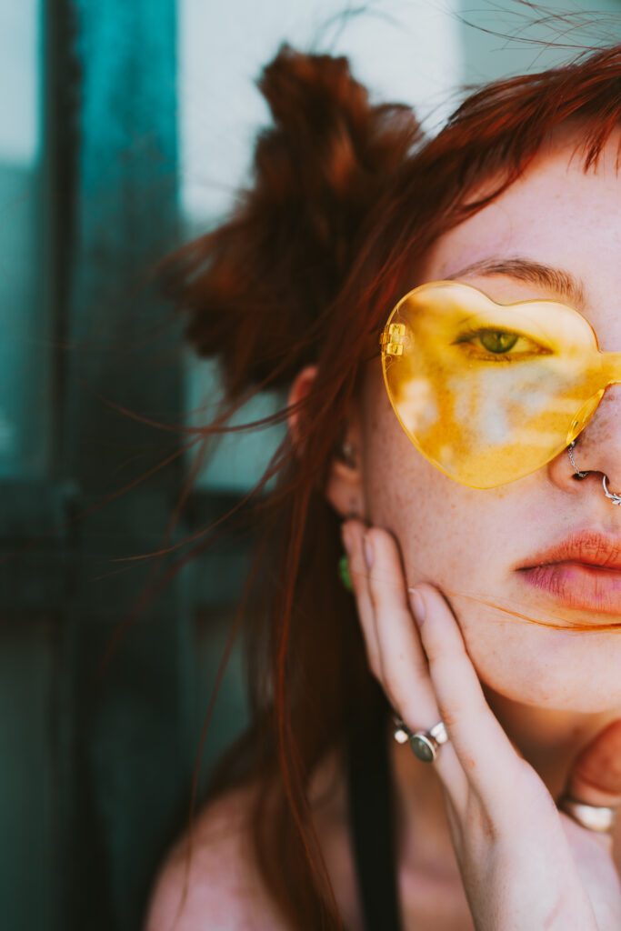 Detail portrait featuring yellow sunglasses and red hair against a teal wall, part of a colorful branding photography session.