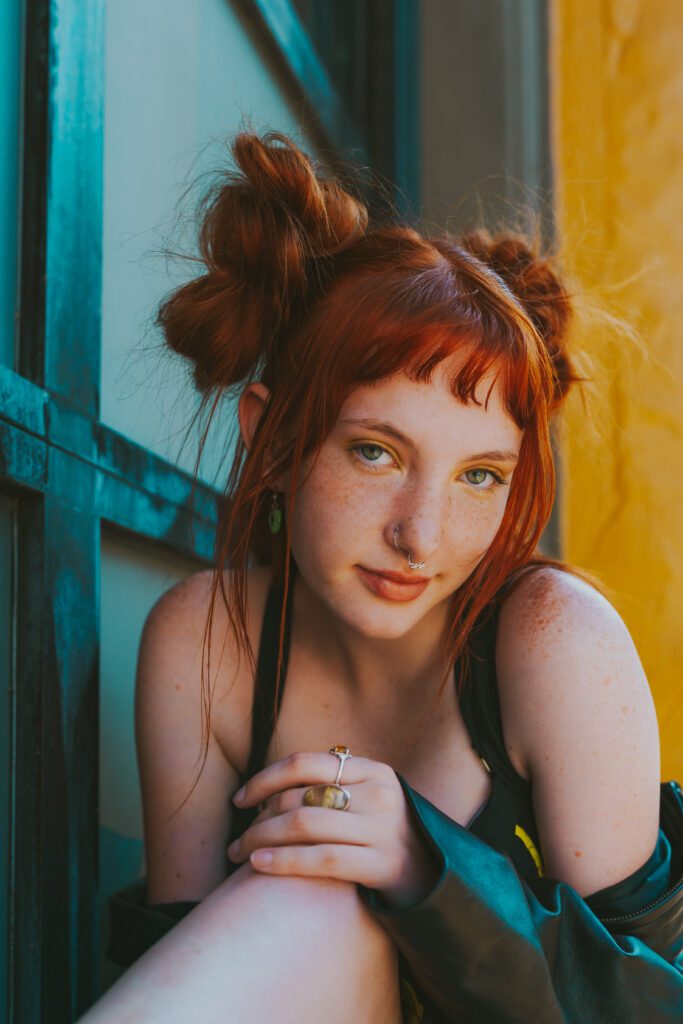 Woman with red hair gazing softly at the camera while framed between teal and yellow panels during a brand photography session in Portland.