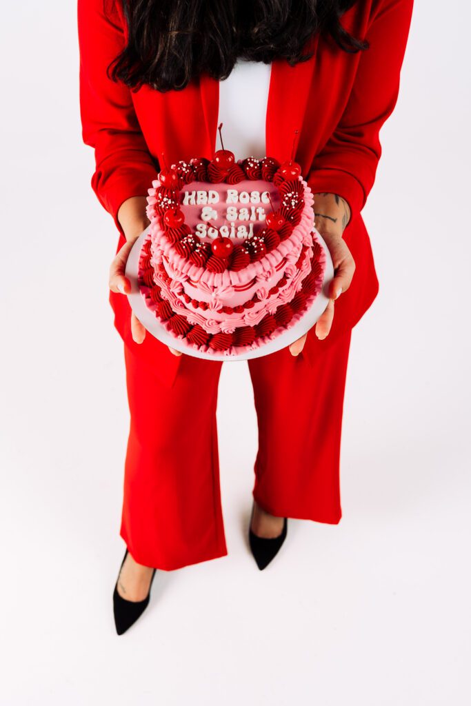 A bold brand photo featuring a woman in a red suit holding a pink heart-shaped cake with cherries, captured from above during a Portland studio session by Mewphotovideo